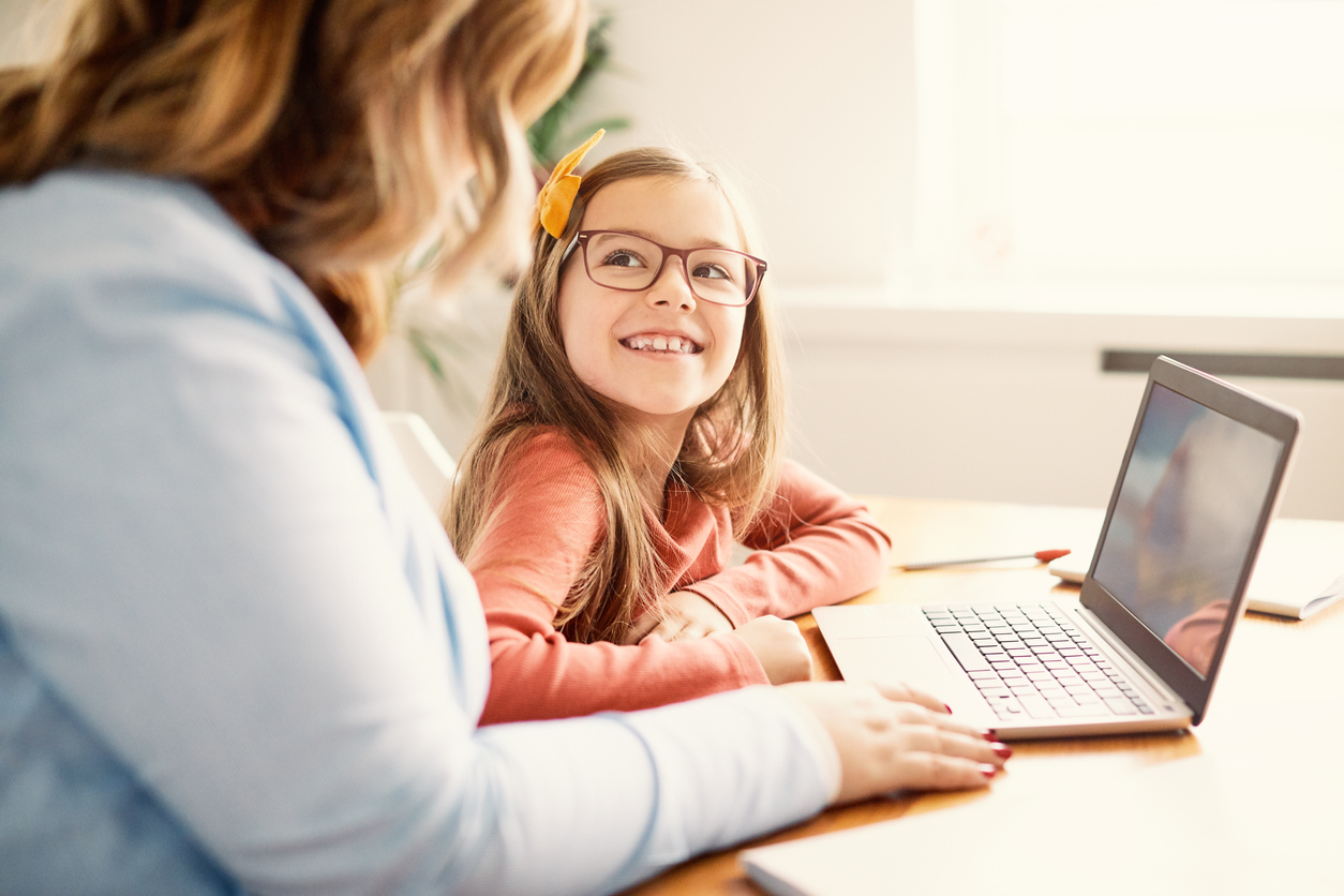 Child and tutor studying together at a table with a laptop 