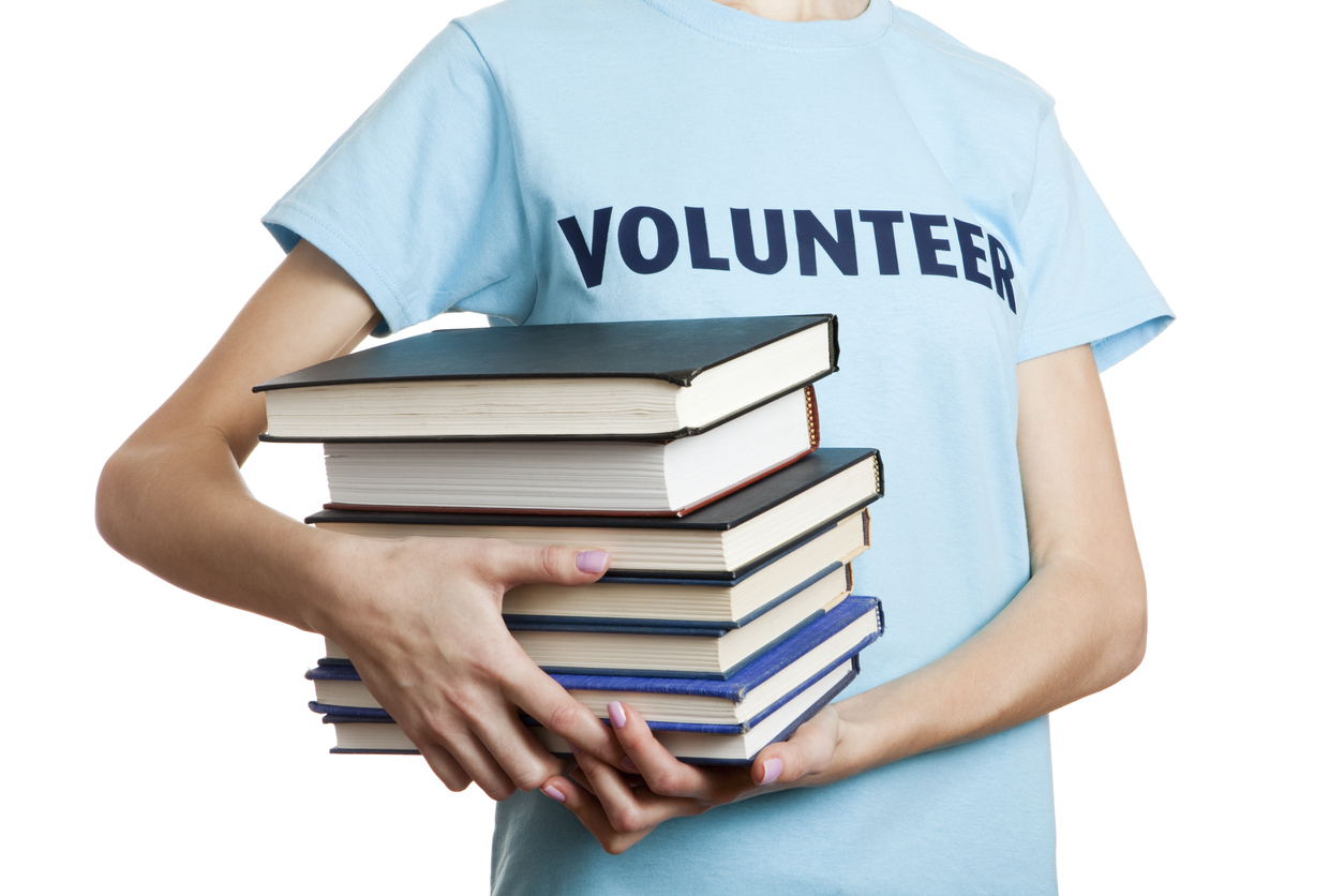 Volunteer holding books with a shirt that has the word volunteer on it.