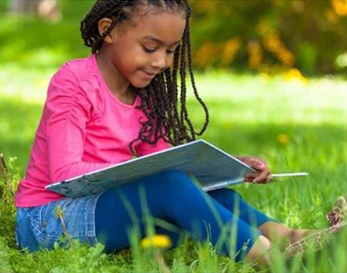 Little girl with pink sweater and long dark hair reading in summer