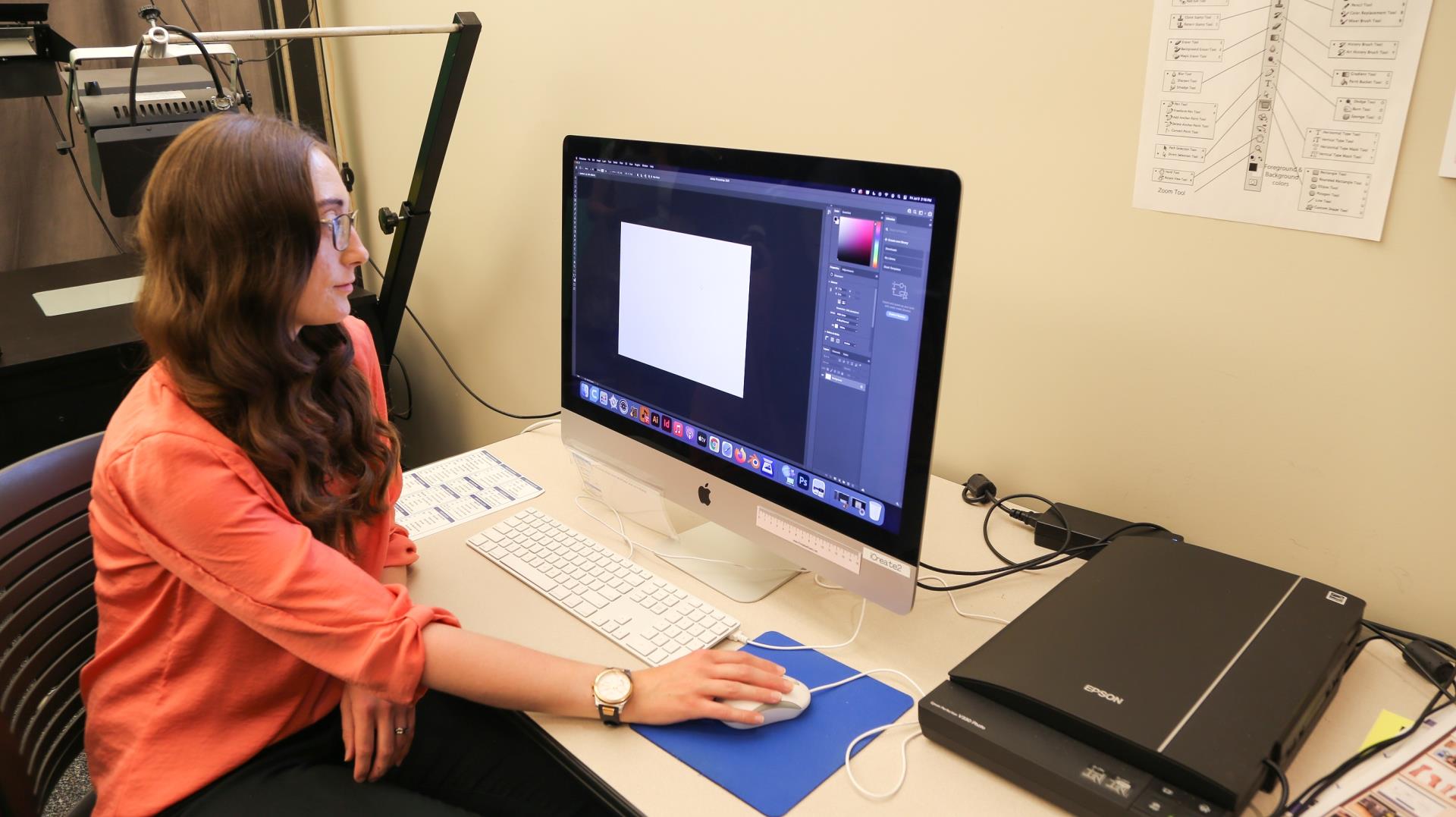 Long haired feminine presenting person using design software on Mac computer