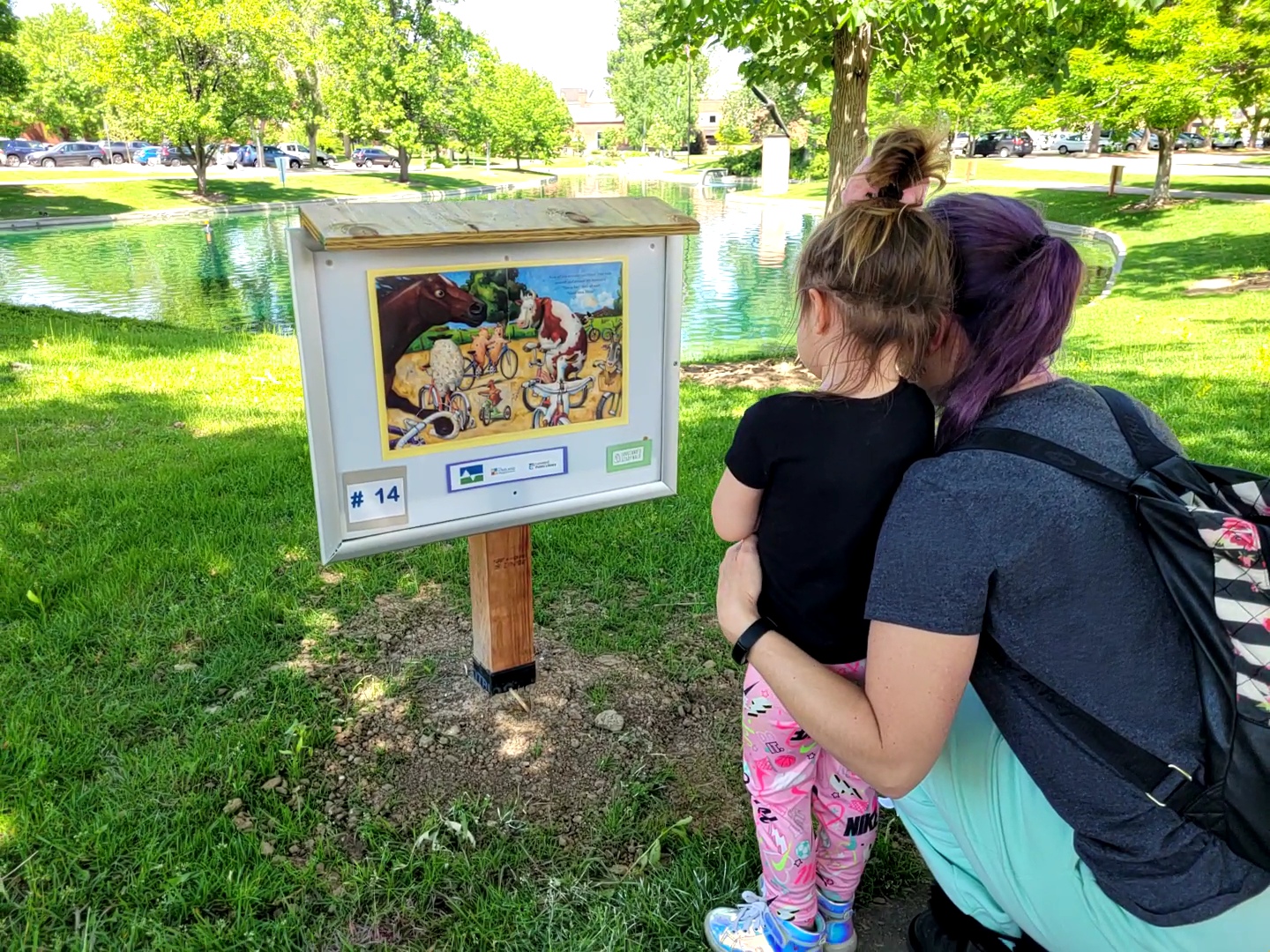 Family looking at storywalk sign around Loveland Library Foote Lagoon