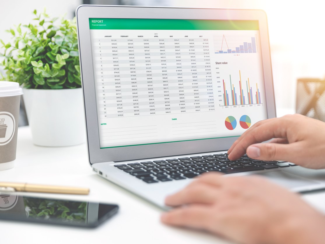 A person using a laptop with a spreadsheet and graphs displayed on the screen