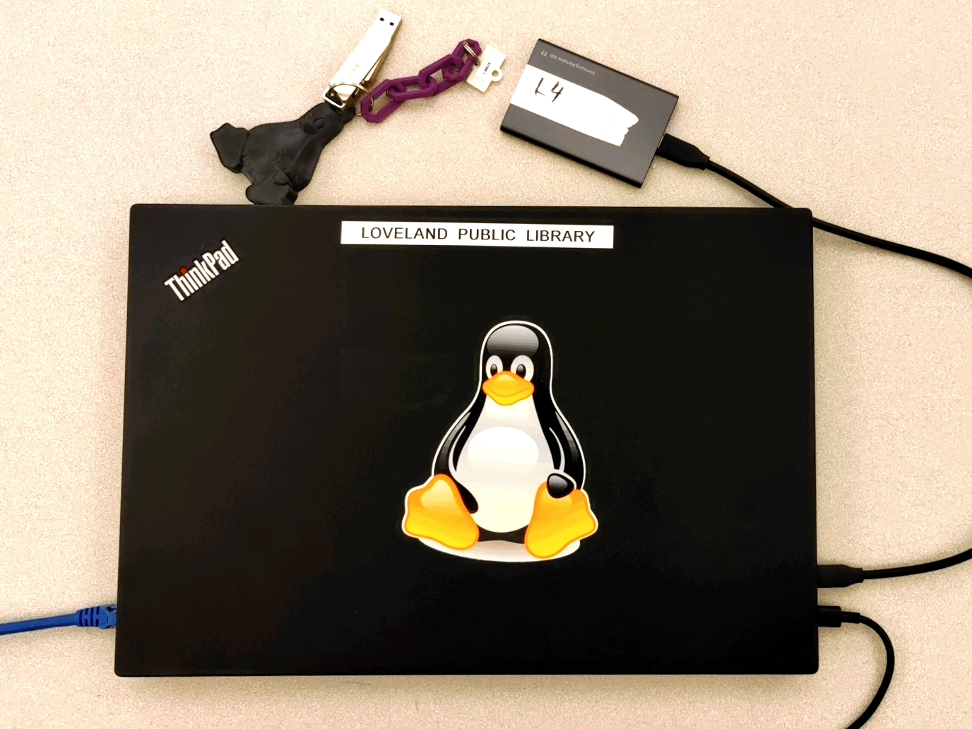 Picture of a laptop with a sticker of the Linux logo and an external hard drive attached