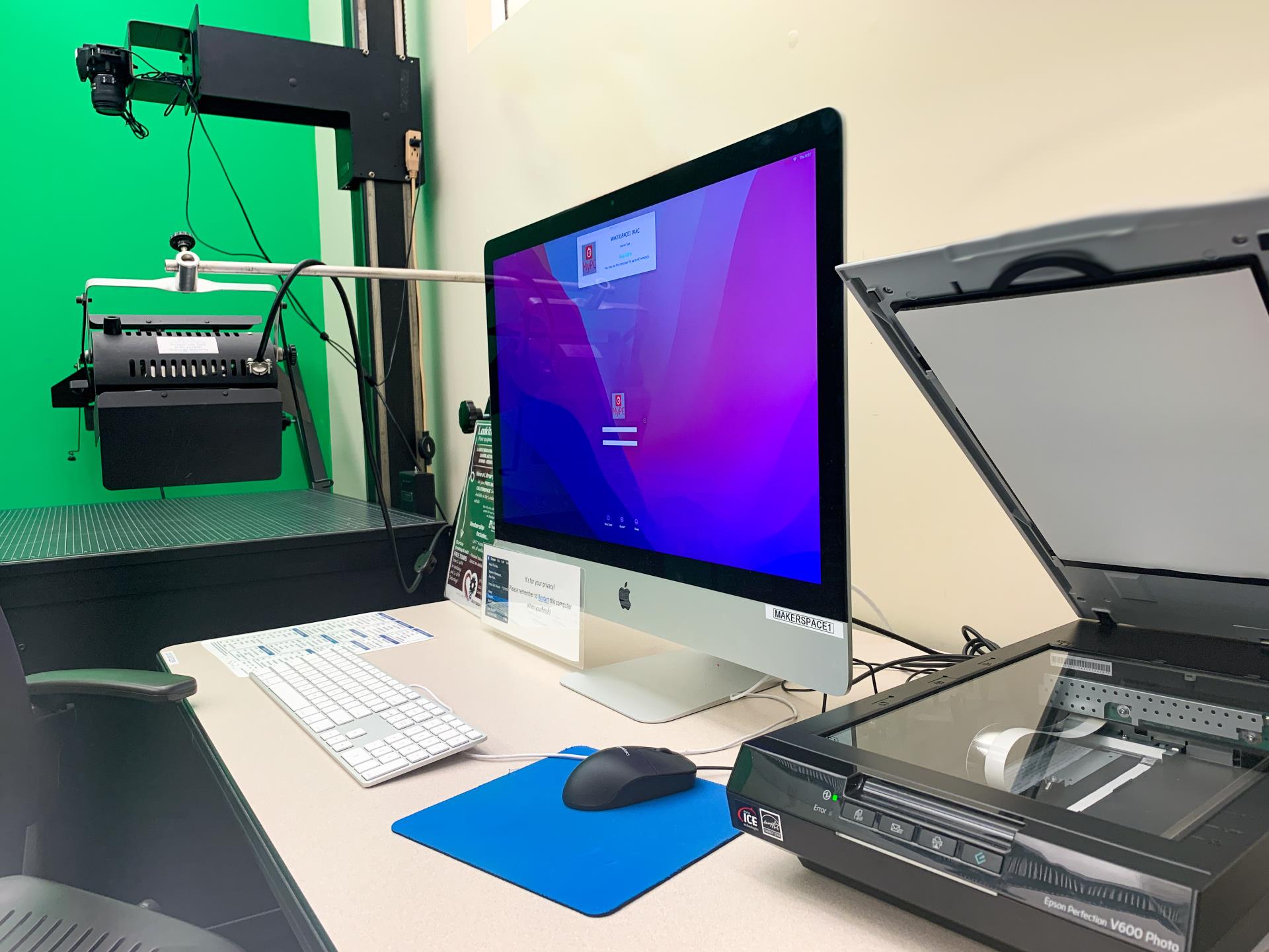 A macintosh computer on a desk with mouse, keyboard and open photo scanner. 2D digitizer camera and greenscreen in background